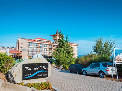 Hotel entrance with parking area, sign, and trees under a clear blue sky.