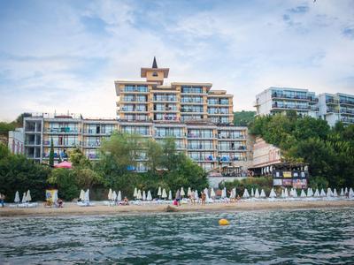 Multi-story hotel building on a beach with sun umbrellas and a wooded surroundings.