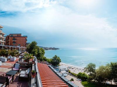 View from a terrace with tables overlooking the sea and a beach under a cloudy sky.