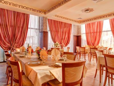 Elegant hotel restaurant with set tables and red curtains on large windows.