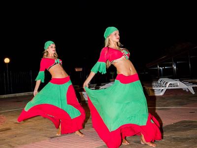 Twee vrouwen dansen 's nachts in rood-groene traditionele jurken op een geplaveid plein.