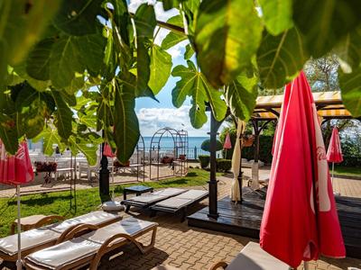 Uitzicht op ligstoelen en rode parasols bij een meer met bergen op de achtergrond.