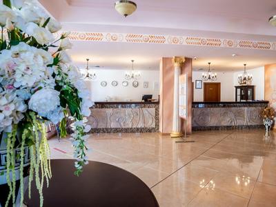 Elegant hotel lobby with reception desk, marble floor, and flower arrangement in foreground.