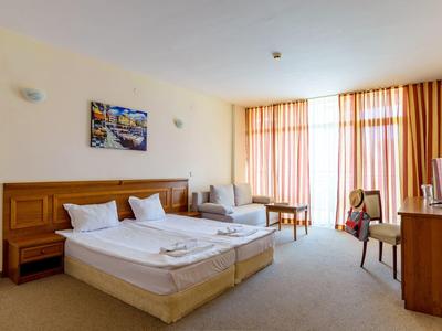 Bright hotel room with two beds, sofa, chairs, and large window with curtains.