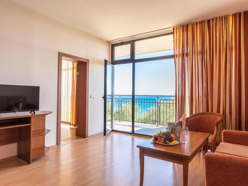 Bright hotel room with sofa, TV, table, and sea view through large windows.