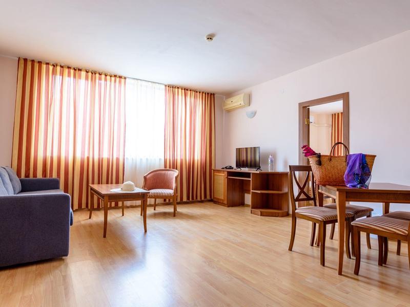 Bright living room with wooden floor, sofa, chairs, and dining table by a window with curtains.