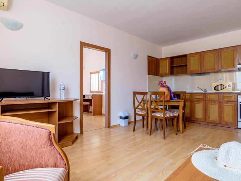 Room with open kitchen, wooden floor, and furniture in warm wood tones.