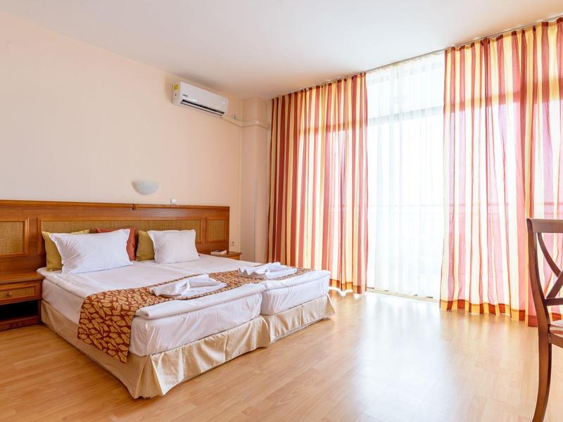 Hotel room with double bed, wooden floor, and large curtains covering floor-to-ceiling windows.