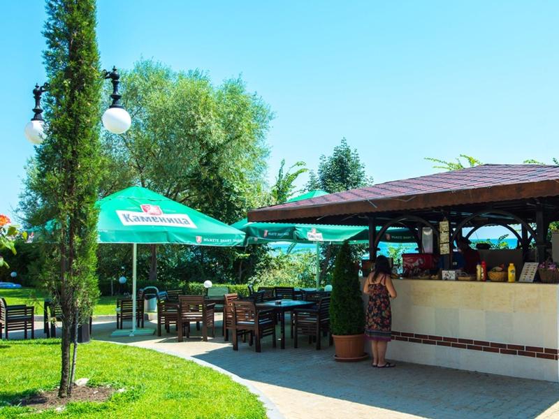 Outdoor bar with seating and green umbrella in sunny garden area.
