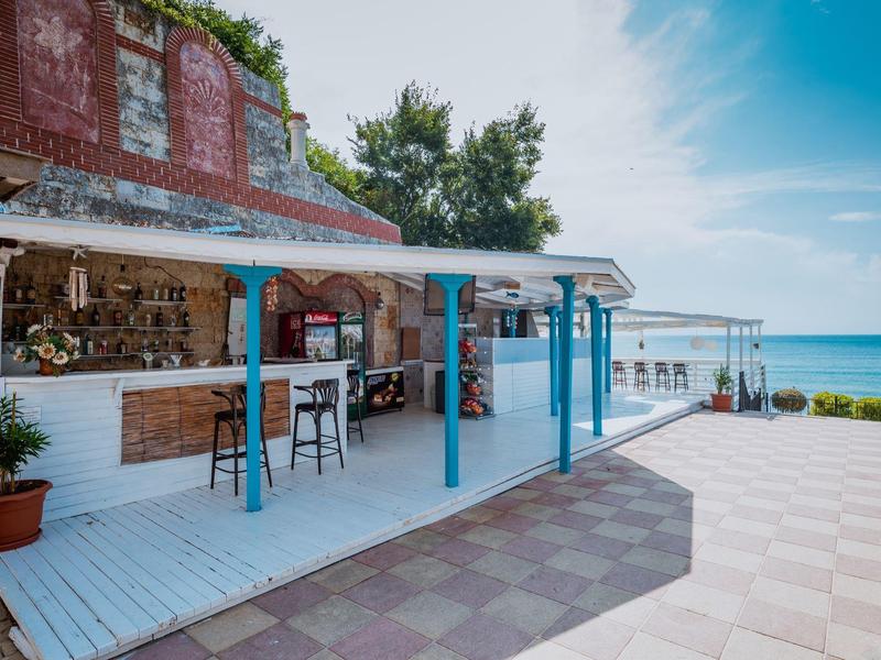 Open beach bar with blue chairs and sea view under clear sky.