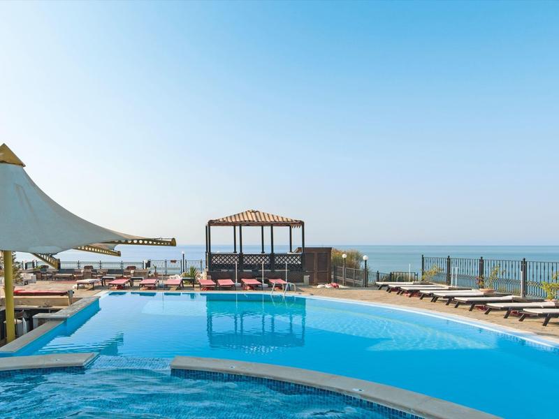 Modern pool area with sea view and sun loungers under clear sky.
