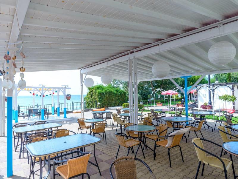 Covered outdoor restaurant area with tables and chairs, view of water in the background.