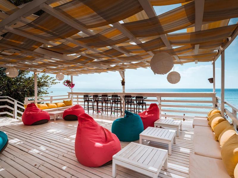 Covered terrace with bean bags, tables, and a view of the sea and beach.