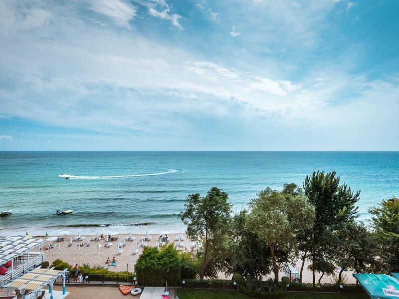 Beach and sea with sunbathers, trees, and cloudy sky