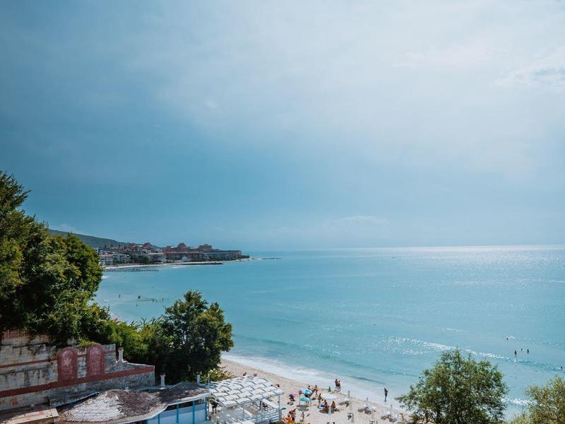 Beach with sunbeds, trees, and a covered area under a blue sky.