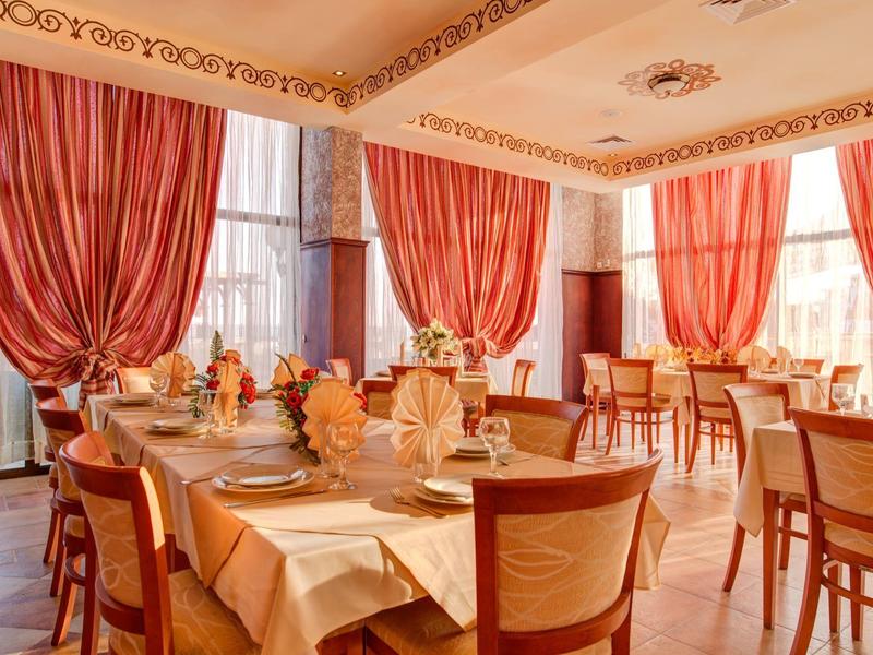 Elegant hotel restaurant with set tables and red curtains on large windows.