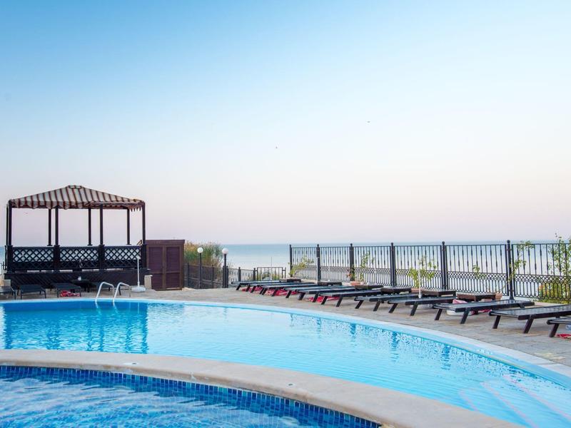 Pool area with loungers and pergola overlooking the sea under clear sky