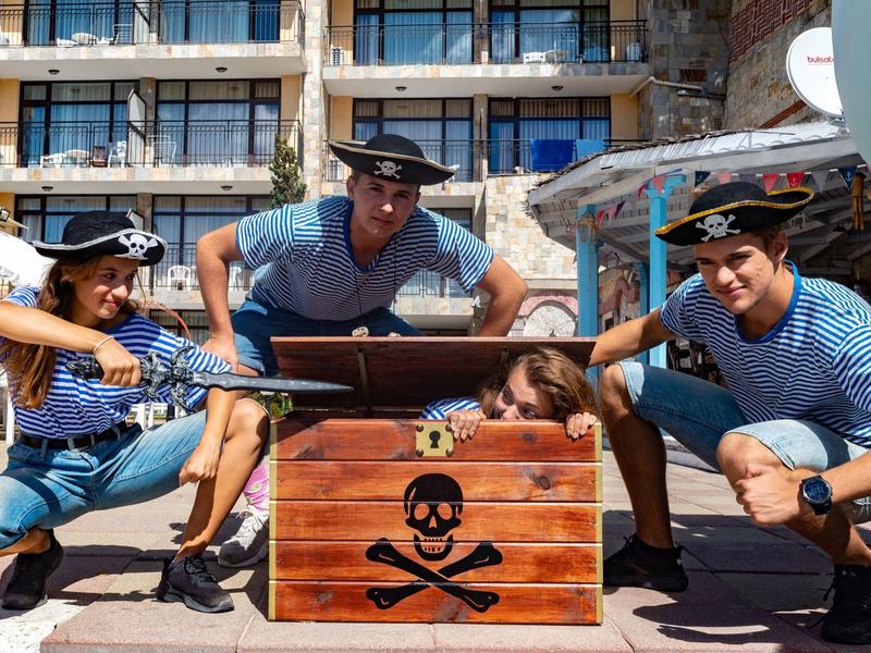 Three people in pirate hats with a treasure chest prop in front of a hotel.