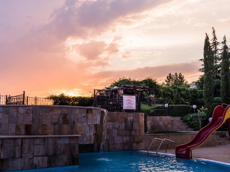 Pool with water slide at sunset and cloudy sky in hotel garden.