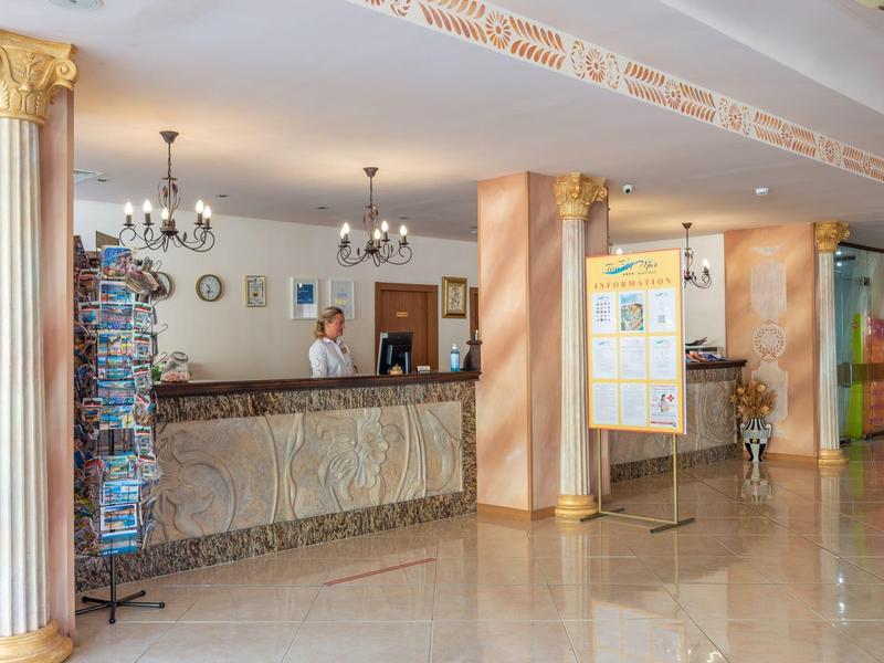 Bright hotel lobby with reception desk, marble floor, and decorative columns.