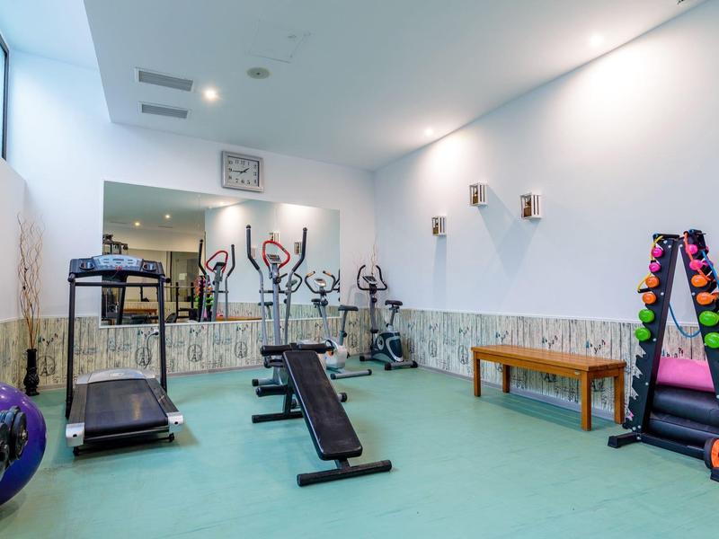 Bright gym with treadmill, dumbbells, workout bench, and wall mirror.