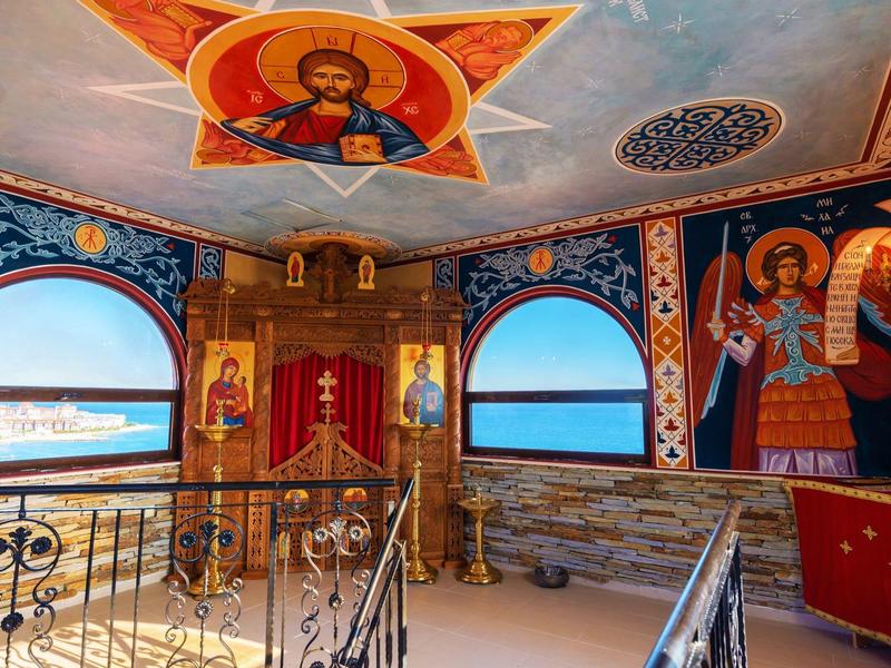 Interior with colorful wall and ceiling paintings and sea view through windows.
