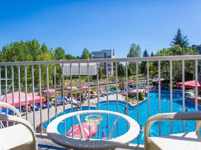 View from a terrace with two chairs and a table overlooking a busy hotel pool with red umbrellas.