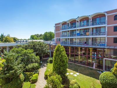 Hotel building with balcony rooms and well-kept garden under clear blue sky.