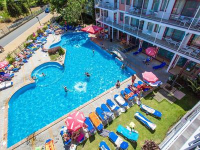 Hotel pool with blue sun loungers and umbrellas, surrounded by hotel buildings and greenery.