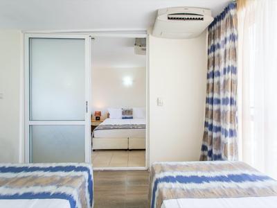 Two single beds with blue and white bedspreads in a bright hotel room overlooking an adjacent bedroom.
