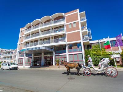 Hotel building with white balconies and a horse-drawn carriage in front under a clear sky