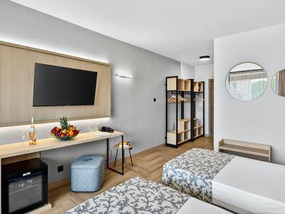 Modernes Hotelzimmer mit zwei Betten, einem Fernseher und einem Holzschrank.