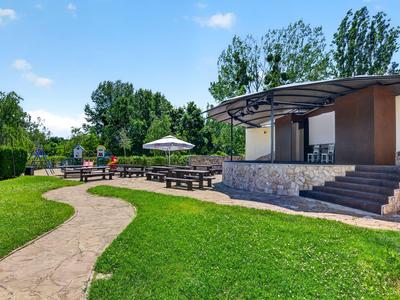 Grüner Gartenbereich mit geschwungenem Weg, Holzsitzbänken und modernem Gebäude mit Terrasse.