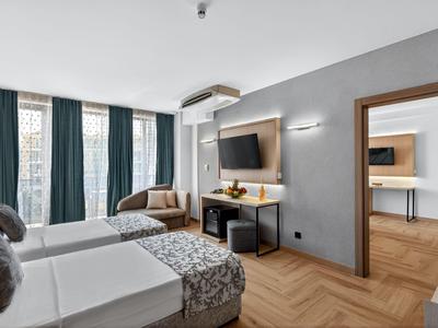 Modernes Hotelzimmer mit zwei Einzelbetten, Fernseher und Sitzbereich bei Tageslicht.