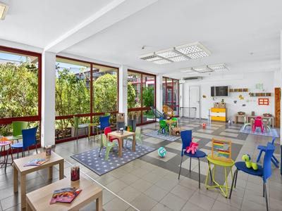 Moderner, heller Speiseraum mit bunten Kindermöbeln und großen Fenstern mit Blick auf Grünflächen.