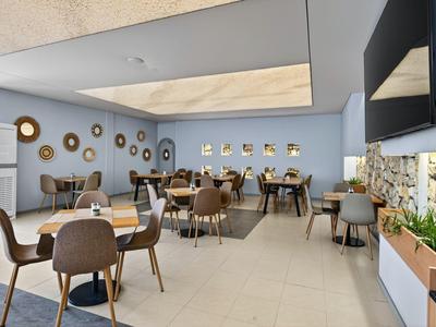 Moderner, geräumiger Speisesaal in einem Hotel mit blau gestrichenen Wänden und vielen Tischen.