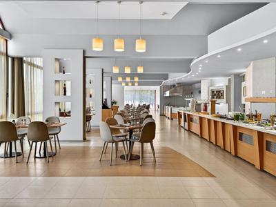 Heller moderner Speisesaal mit Tischen, Stühlen und Buffetbereich in einem Hotel.