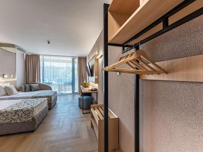 Nowoczesny pokój hotelowy z łóżkiem podwójnym, sofą, biurkiem i otwartym stojakiem na ubrania.
