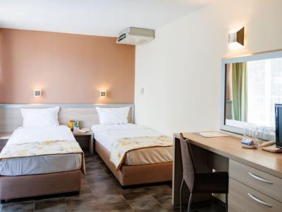 Jasny pokój hotelowy z dwoma łóżkami pojedynczymi, biurkiem i dużym lustrem na ścianie.