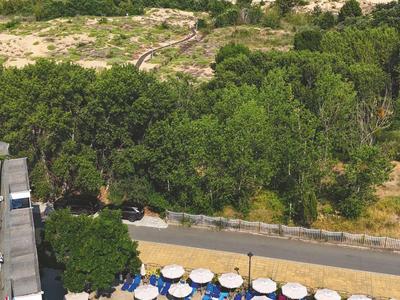 Basen hotelowy z parasolami, za nimi zielona roślinność i morze w tle.