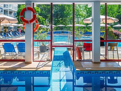 Widok na baseny wewnętrzne i zewnętrzne z niebieskimi leżakami i parasolami w hotelu.