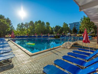 Piscina all'aperto soleggiata con lettini blu e ombrelloni rossi.