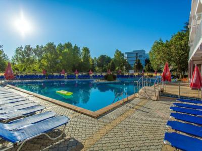 Sunny outdoor pool with lounge chairs and red umbrellas in a hotel garden.