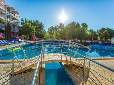 Piccolo ponte su una piscina all'aperto con lettini e alberi in una giornata di sole.