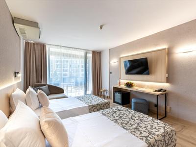 Nowoczesny pokój hotelowy z dwoma łóżkami, telewizorem, biurkiem i dużymi oknami.