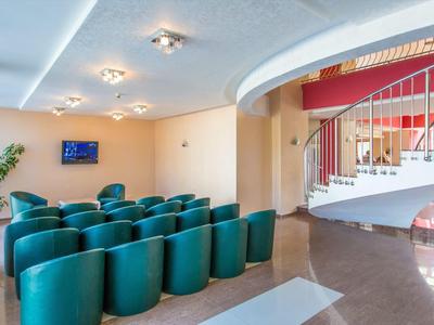 Modern lounge area with green chairs and spiral staircase in bright hotel interior.