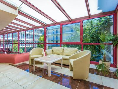 Cozy seating area with light armchairs and sofa in a glassed hotel corridor.