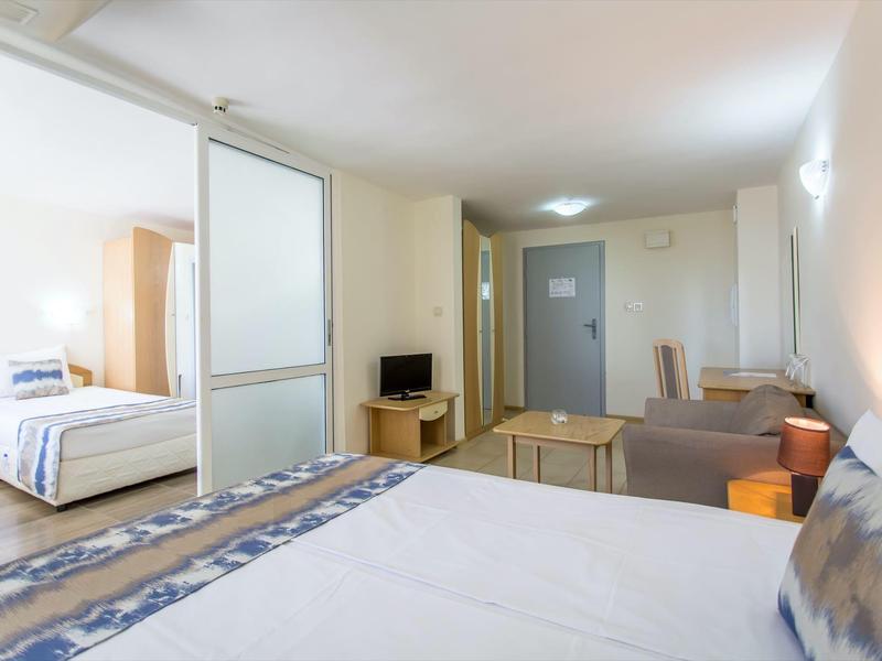 Bright hotel room with two bedrooms, sofas, and a small TV.