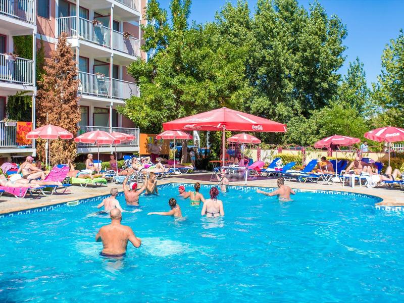 Busy hotel pool with sun umbrellas and guests swimming in clear blue water.