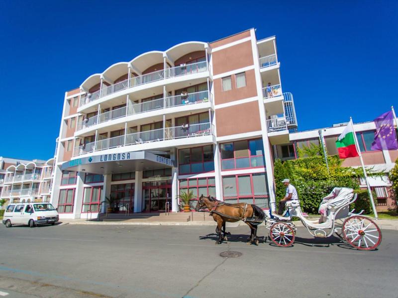 Hotel building with white balconies and a horse-drawn carriage in front under a clear sky